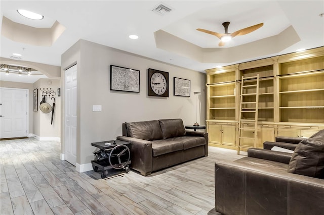 living room with ceiling fan, a tray ceiling, and light hardwood / wood-style floors