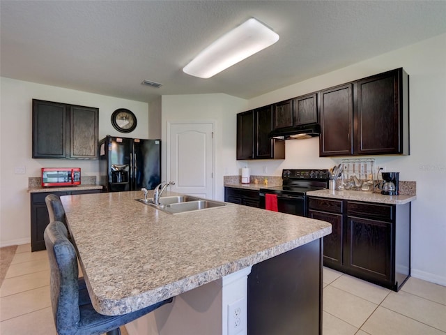 kitchen with black appliances, sink, light tile patterned floors, and a kitchen island with sink