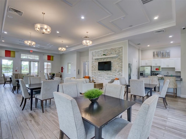 dining room with ornamental molding, a raised ceiling, a notable chandelier, and light hardwood / wood-style flooring