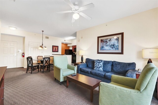 living room with ceiling fan with notable chandelier and dark carpet