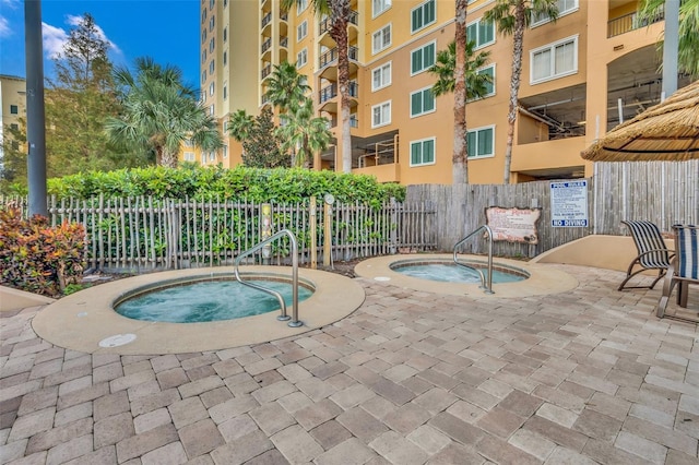 view of swimming pool with a patio, a community hot tub, and fence