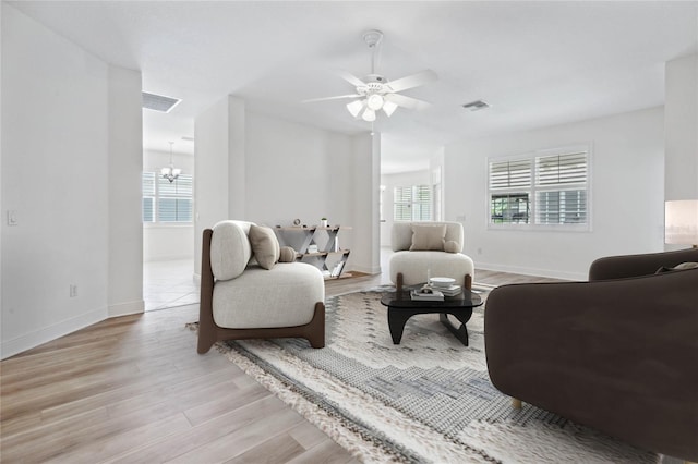 living room with light wood-type flooring and ceiling fan with notable chandelier