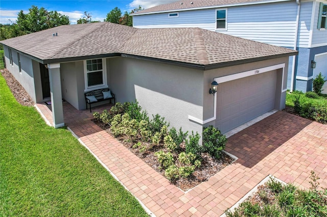 view of property exterior featuring stucco siding, a lawn, decorative driveway, an attached garage, and a shingled roof