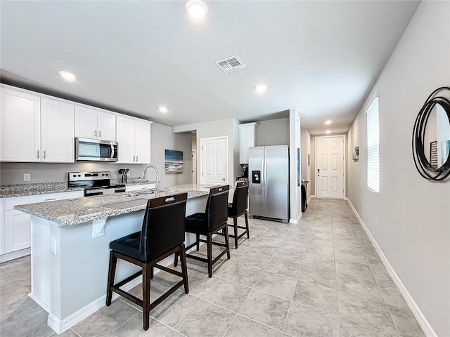 kitchen with visible vents, light stone counters, a kitchen breakfast bar, white cabinetry, and appliances with stainless steel finishes