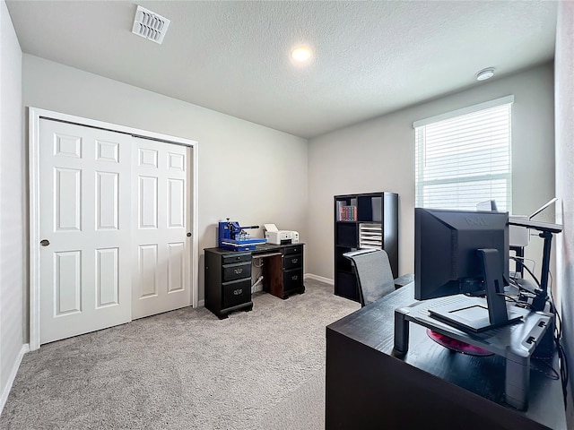 office space featuring light carpet, visible vents, a textured ceiling, and baseboards