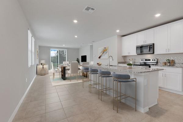 kitchen featuring visible vents, appliances with stainless steel finishes, a center island with sink, and white cabinetry