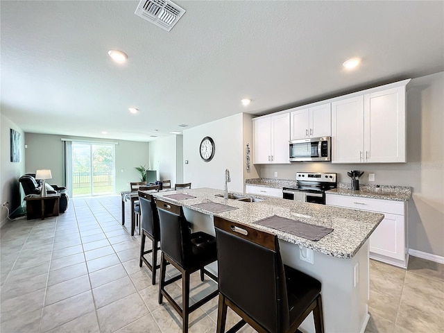 kitchen featuring visible vents, a sink, light stone counters, appliances with stainless steel finishes, and a kitchen island with sink