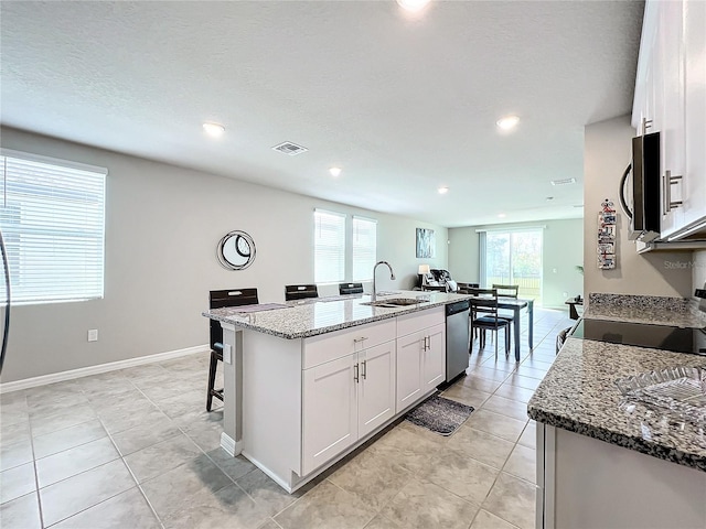 kitchen featuring light stone countertops, a center island with sink, visible vents, a sink, and appliances with stainless steel finishes