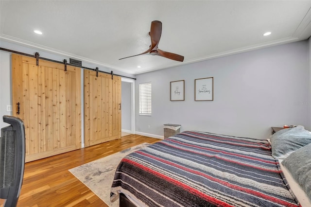 bedroom with a barn door, ceiling fan, ornamental molding, and hardwood / wood-style floors