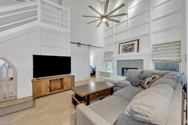 tiled living room with a barn door, ceiling fan, and a high ceiling