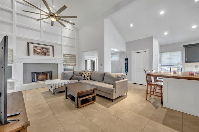 living room featuring high vaulted ceiling, light tile patterned floors, ceiling fan, and a tile fireplace