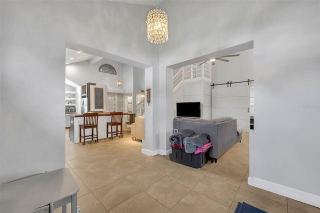 tiled living room featuring a barn door, ceiling fan with notable chandelier, and high vaulted ceiling