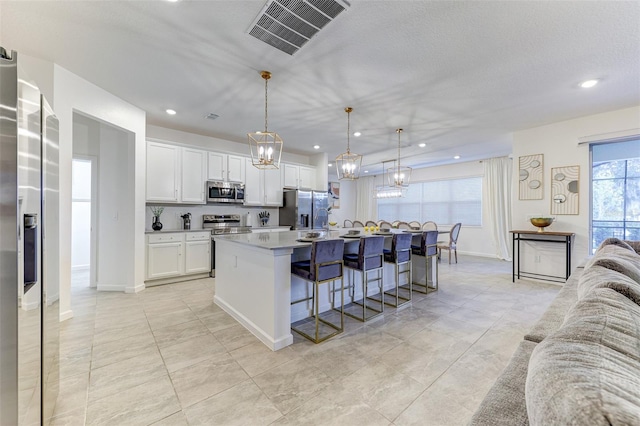 kitchen with a center island with sink, appliances with stainless steel finishes, a breakfast bar, hanging light fixtures, and white cabinets