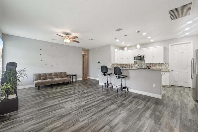 kitchen featuring hardwood / wood-style floors, white cabinetry, backsplash, appliances with stainless steel finishes, and a breakfast bar area