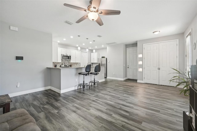 kitchen with wood-type flooring, appliances with stainless steel finishes, kitchen peninsula, ceiling fan, and white cabinets