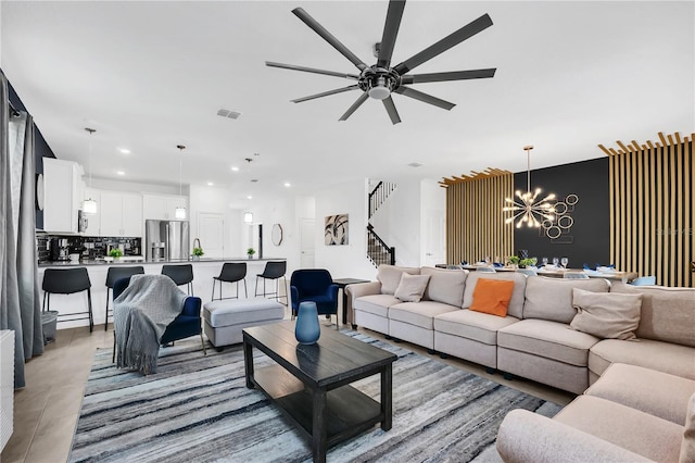 tiled living room with ceiling fan with notable chandelier