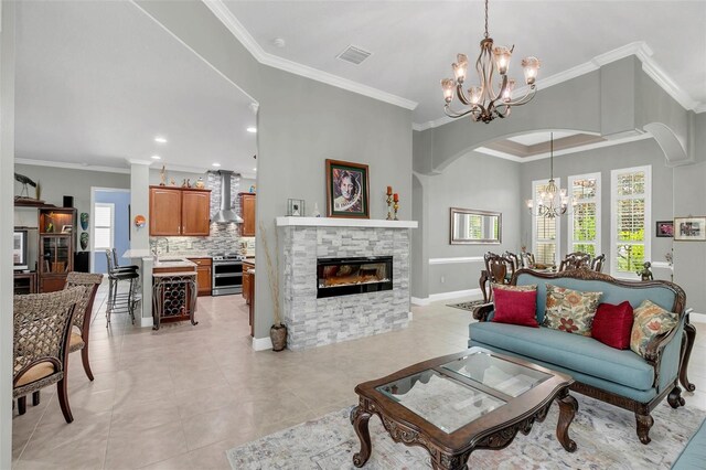 living room with crown molding, a wealth of natural light, an inviting chandelier, and a stone fireplace