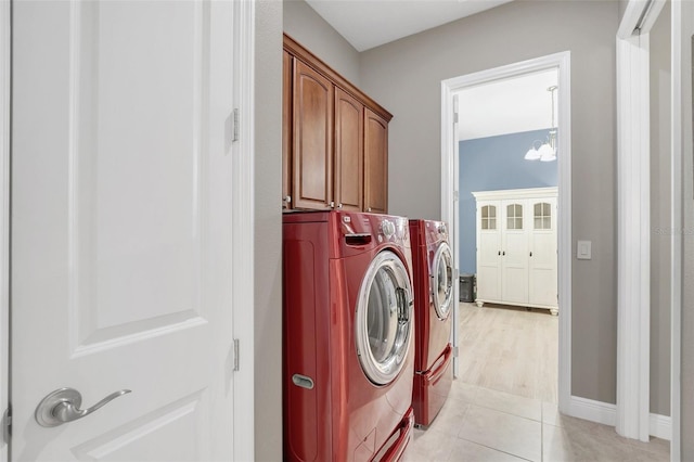 laundry area with washing machine and clothes dryer, cabinets, a notable chandelier, and light tile patterned floors