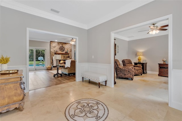 sitting room with wood-type flooring, a stone fireplace, ceiling fan, and crown molding