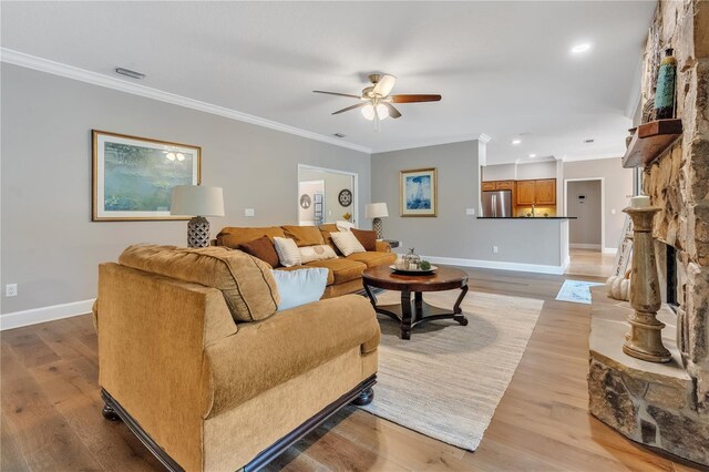 living room with a stone fireplace, crown molding, light hardwood / wood-style flooring, and ceiling fan