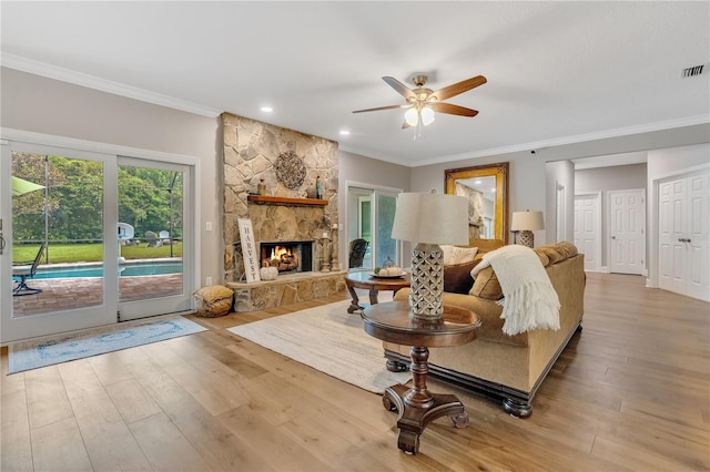 living room with ornamental molding, ceiling fan, light wood-type flooring, and a stone fireplace