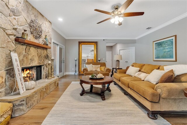 living room with light hardwood / wood-style floors, a stone fireplace, ceiling fan, and crown molding