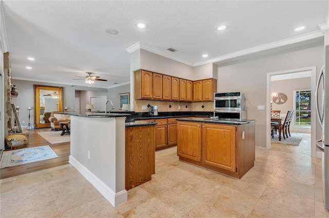 kitchen with kitchen peninsula, ornamental molding, ceiling fan, and a kitchen island