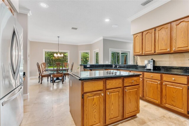 kitchen with dark stone countertops, stainless steel fridge, crown molding, a textured ceiling, and decorative light fixtures