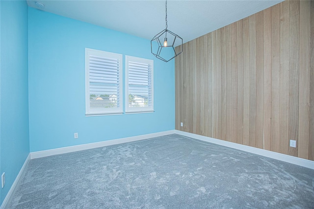 carpeted empty room with wooden walls and a notable chandelier