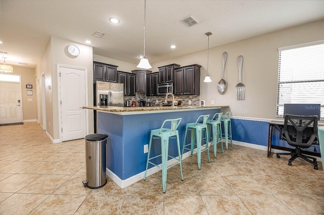 kitchen with tasteful backsplash, a kitchen bar, kitchen peninsula, hanging light fixtures, and appliances with stainless steel finishes