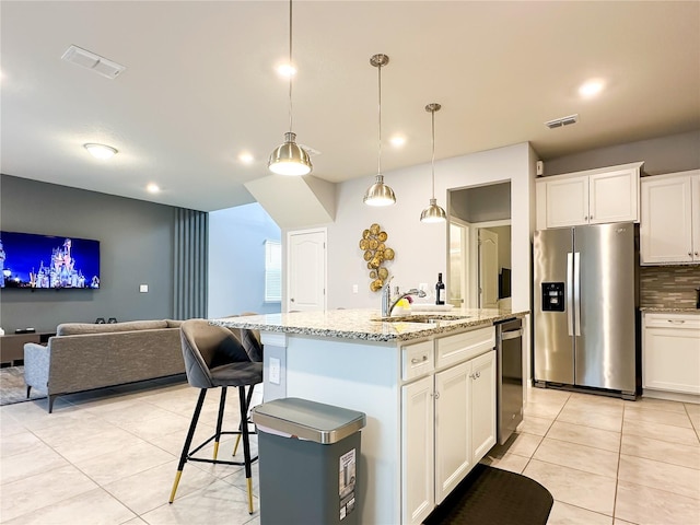 kitchen with white cabinetry, backsplash, light tile patterned floors, stainless steel appliances, and a center island with sink