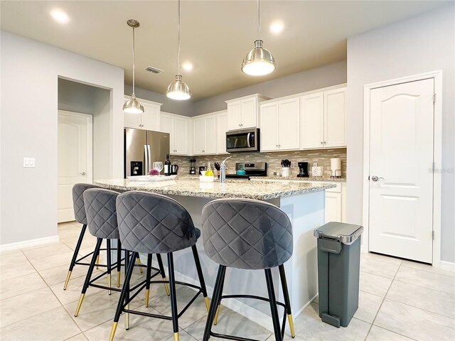 kitchen featuring white cabinets, backsplash, stainless steel appliances, light tile patterned flooring, and a center island with sink