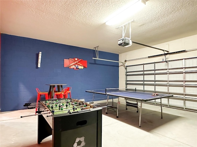 recreation room with a garage, concrete block wall, concrete floors, and a textured ceiling