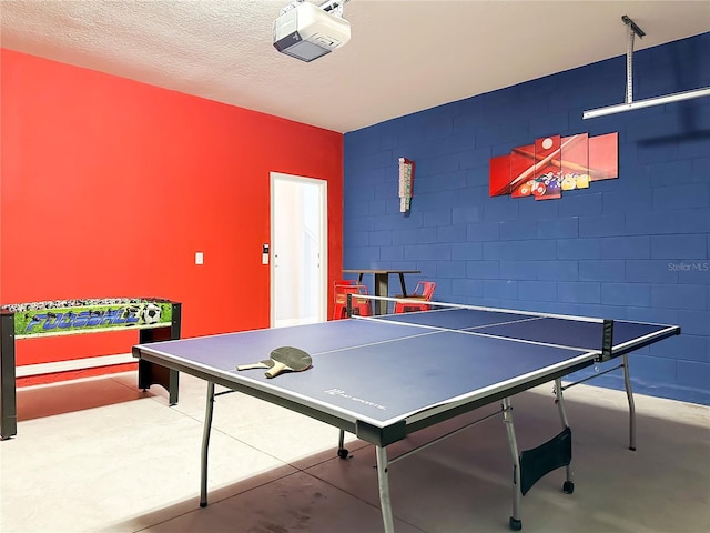 rec room with concrete flooring, concrete block wall, and a textured ceiling