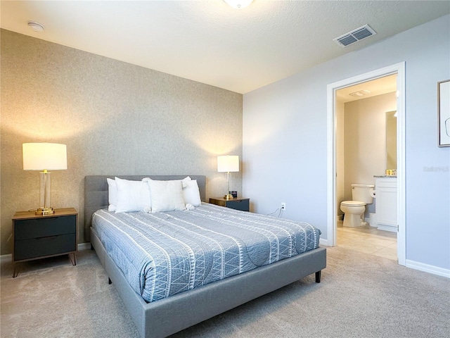 carpeted bedroom featuring connected bathroom, visible vents, and baseboards