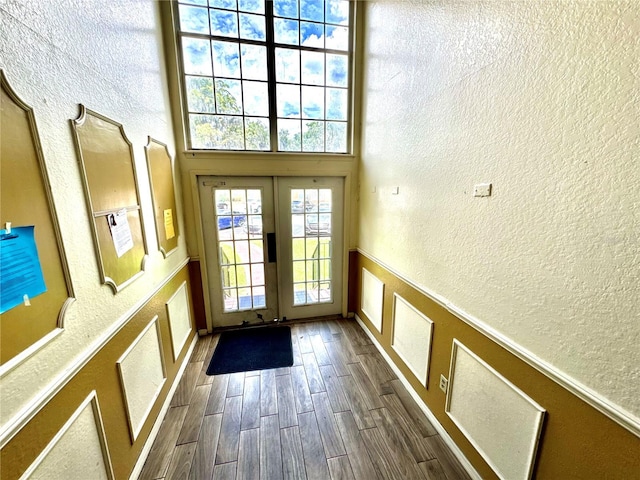 entryway featuring french doors, a textured wall, a wainscoted wall, and dark wood-type flooring