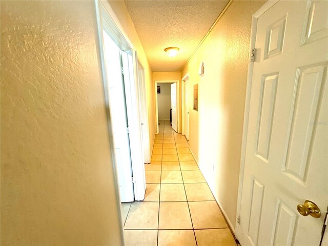 hall with a textured wall, a textured ceiling, and light tile patterned floors