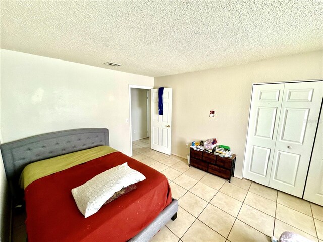 bedroom featuring a closet, a textured ceiling, visible vents, and light tile patterned floors