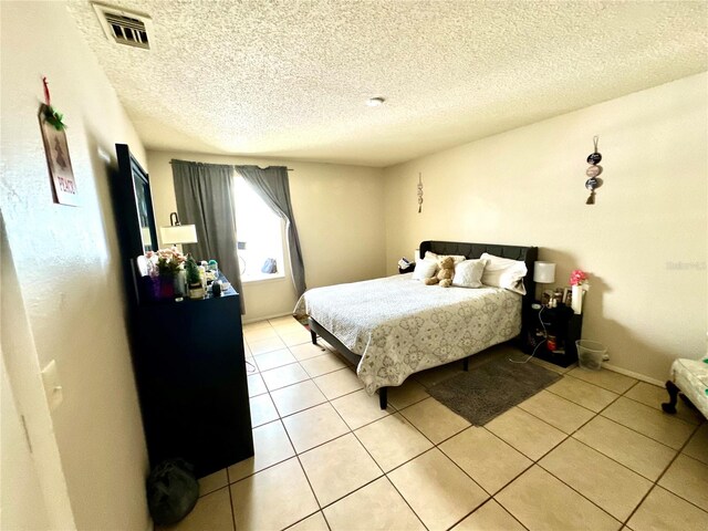 bedroom featuring baseboards, visible vents, a textured ceiling, and light tile patterned flooring
