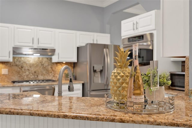 kitchen featuring light stone counters, white cabinets, stainless steel appliances, a fireplace, and backsplash