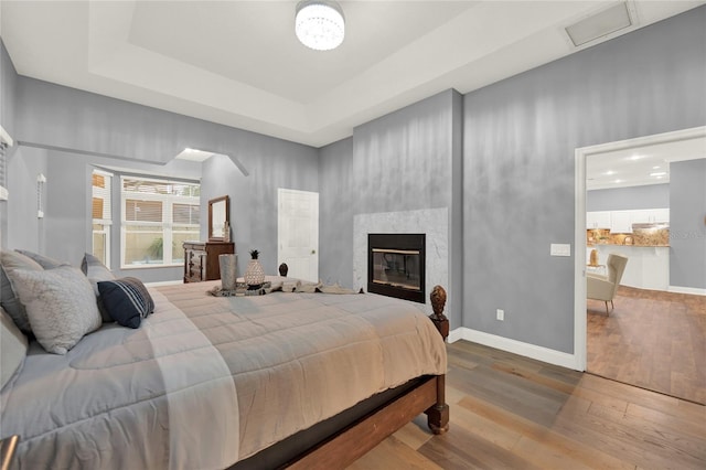 bedroom featuring hardwood / wood-style flooring, a large fireplace, and a raised ceiling