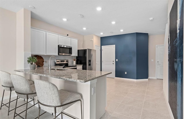 kitchen featuring light tile patterned floors, stainless steel appliances, light stone counters, sink, and white cabinets