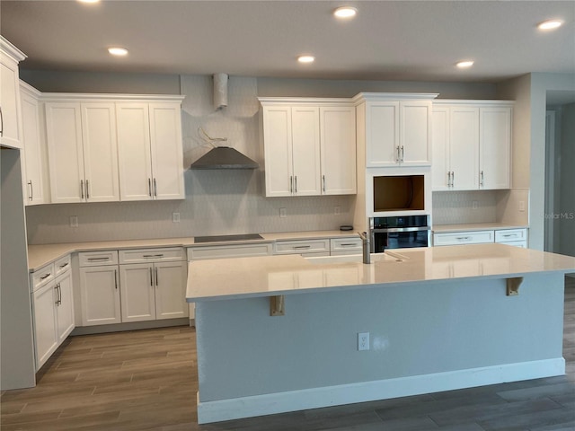 kitchen featuring dark hardwood / wood-style flooring, a kitchen island with sink, white cabinets, and wall oven