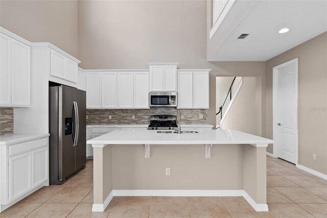 kitchen featuring visible vents, an island with sink, appliances with stainless steel finishes, a kitchen breakfast bar, and a sink