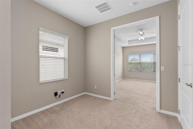 spare room featuring baseboards, a ceiling fan, visible vents, and light colored carpet