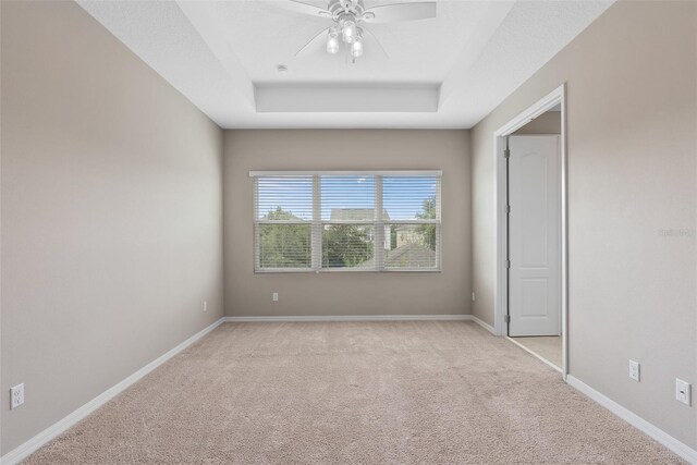 empty room with baseboards, a tray ceiling, a ceiling fan, and light colored carpet