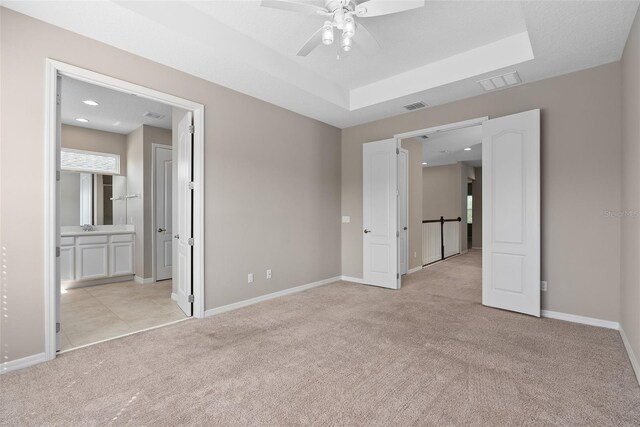 spare room with baseboards, a tray ceiling, visible vents, and light colored carpet