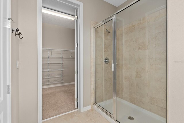 full bath featuring a spacious closet, tile patterned flooring, a shower stall, and baseboards