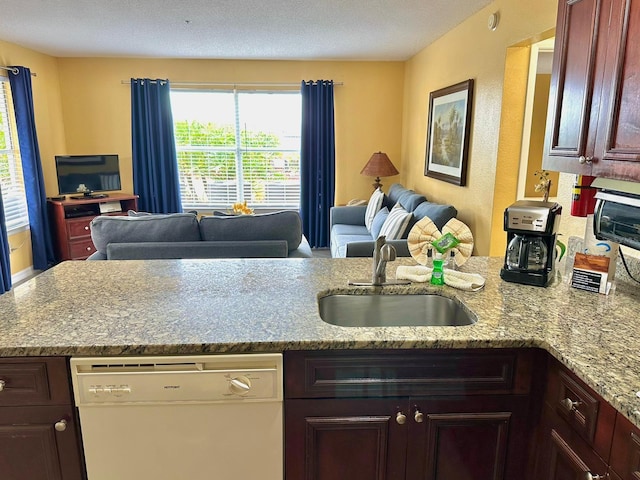 kitchen featuring open floor plan, a peninsula, light stone countertops, white dishwasher, and a sink