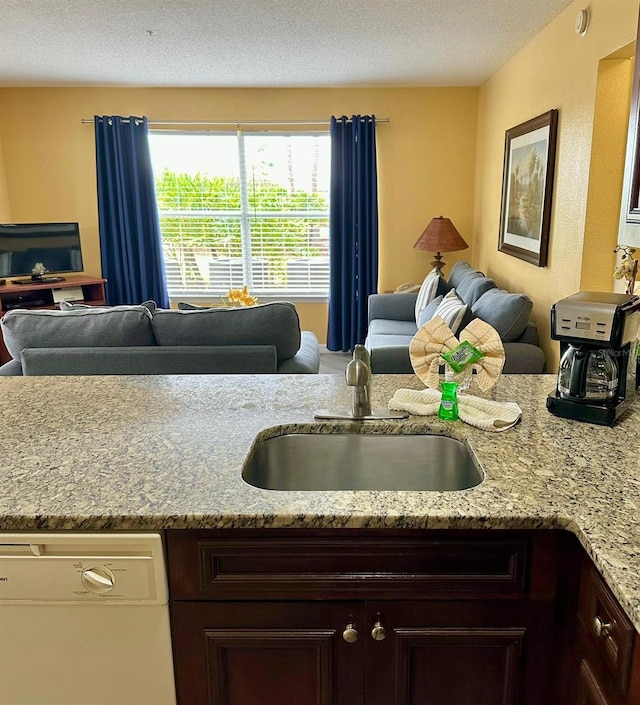 kitchen featuring dishwasher, light stone counters, open floor plan, dark brown cabinets, and a sink